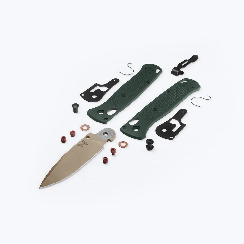 Disassembled knife kit with green handle scales, blade, screws, and small hardware laid out on a white background, ready for assembly.