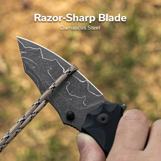 Close-up of a razor-sharp Damascus steel knife blade held by a hand against a blurred outdoor background.