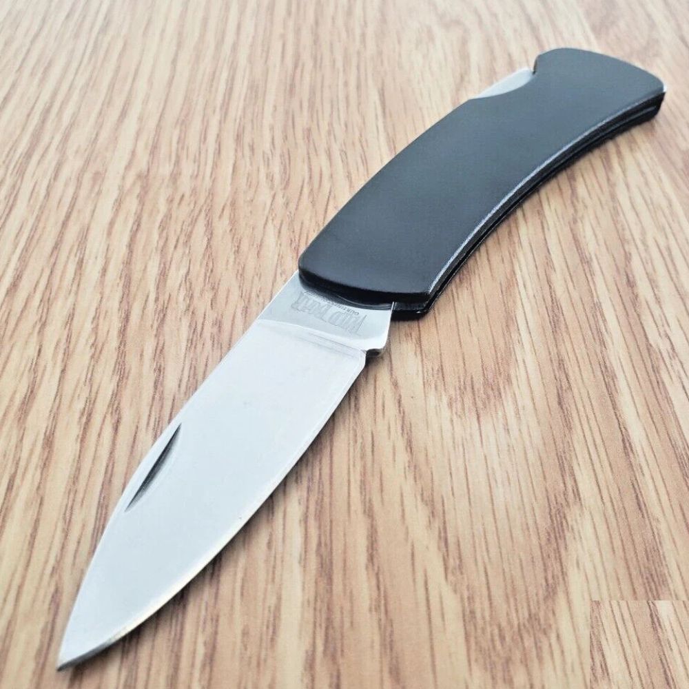 Folding knife with a black handle opened on a wooden surface, blade partially extended.