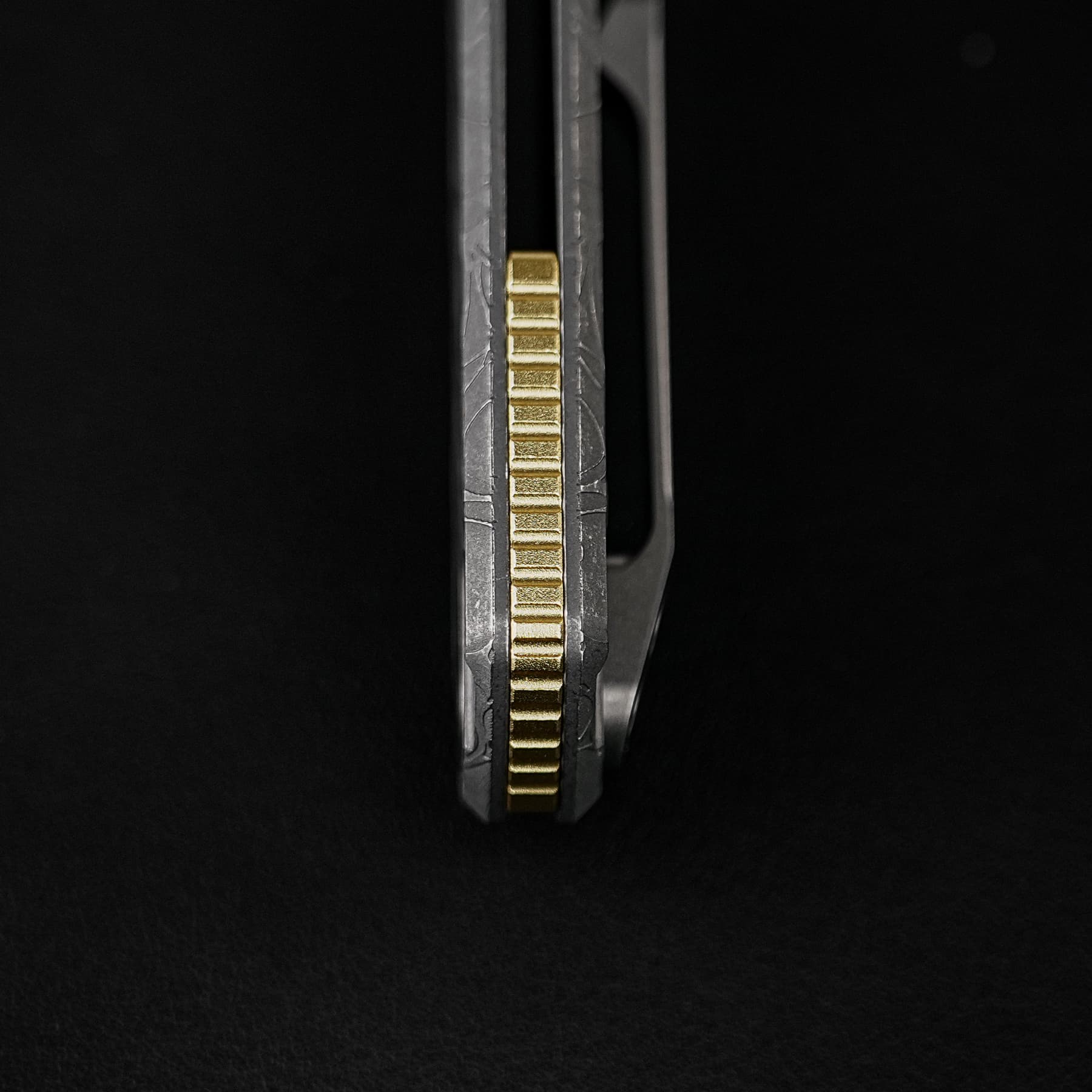 Close-up of a gold grooved strip between dark metal parts against a black background.
