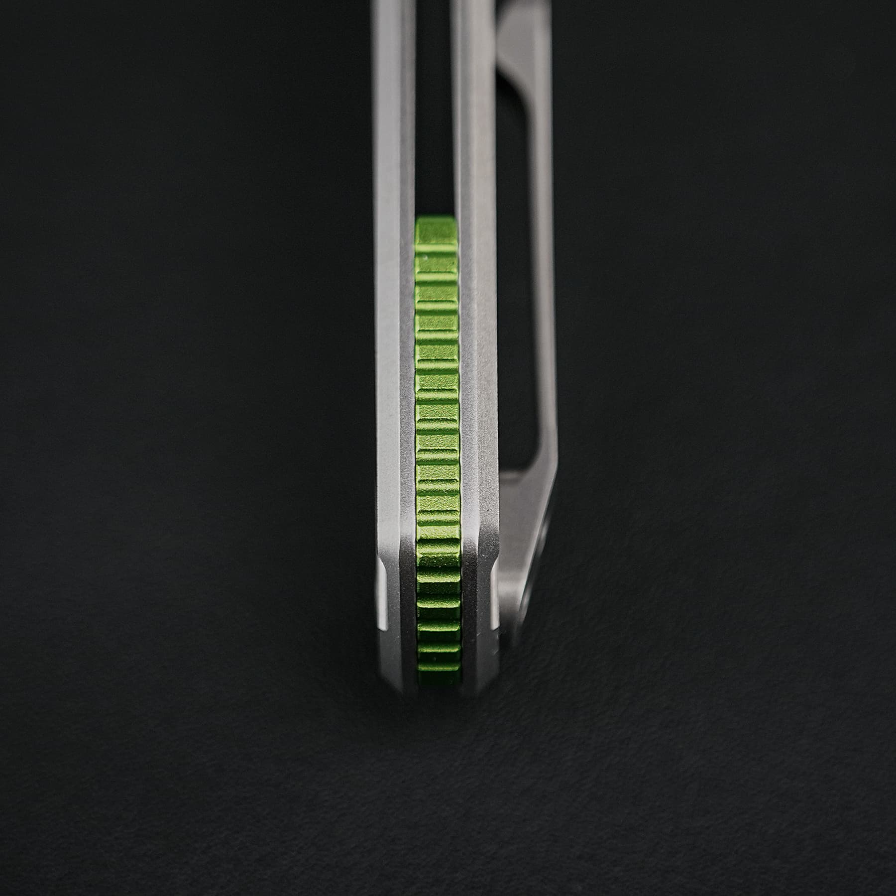 Close-up of a lime-green knurled edge between two gray metal rails against a dark background.