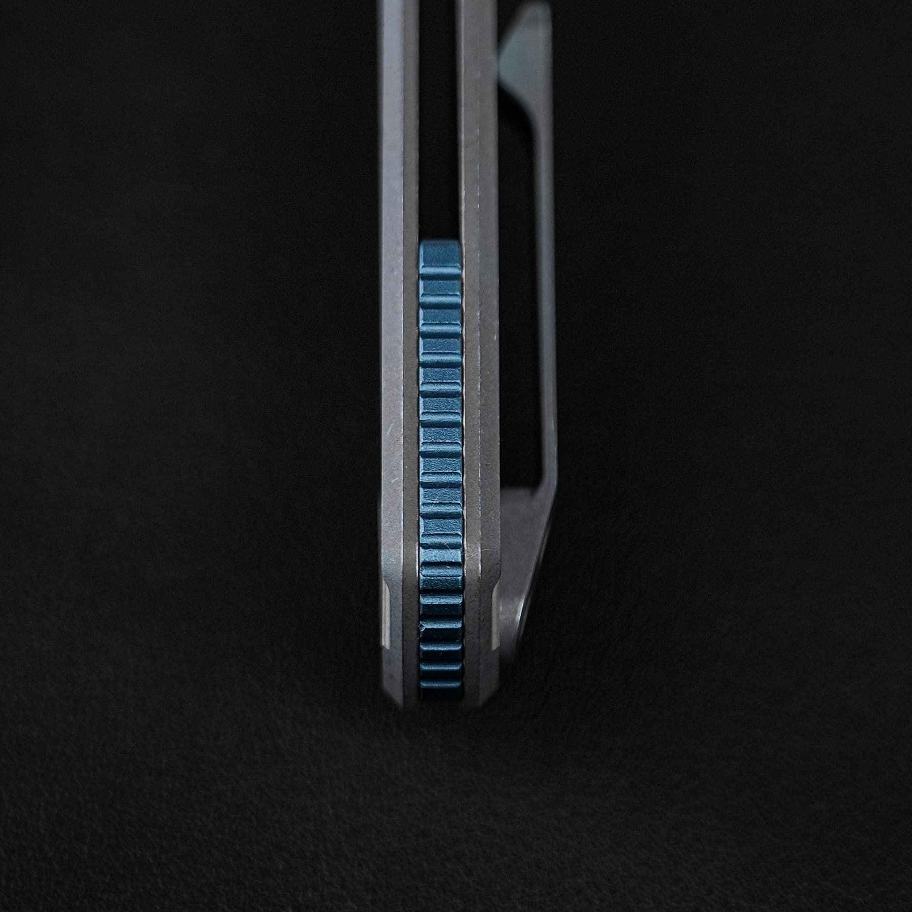 Close-up of a blue, ribbed adjustment knob set between two vertical metal rails against a black background, viewed from above.
