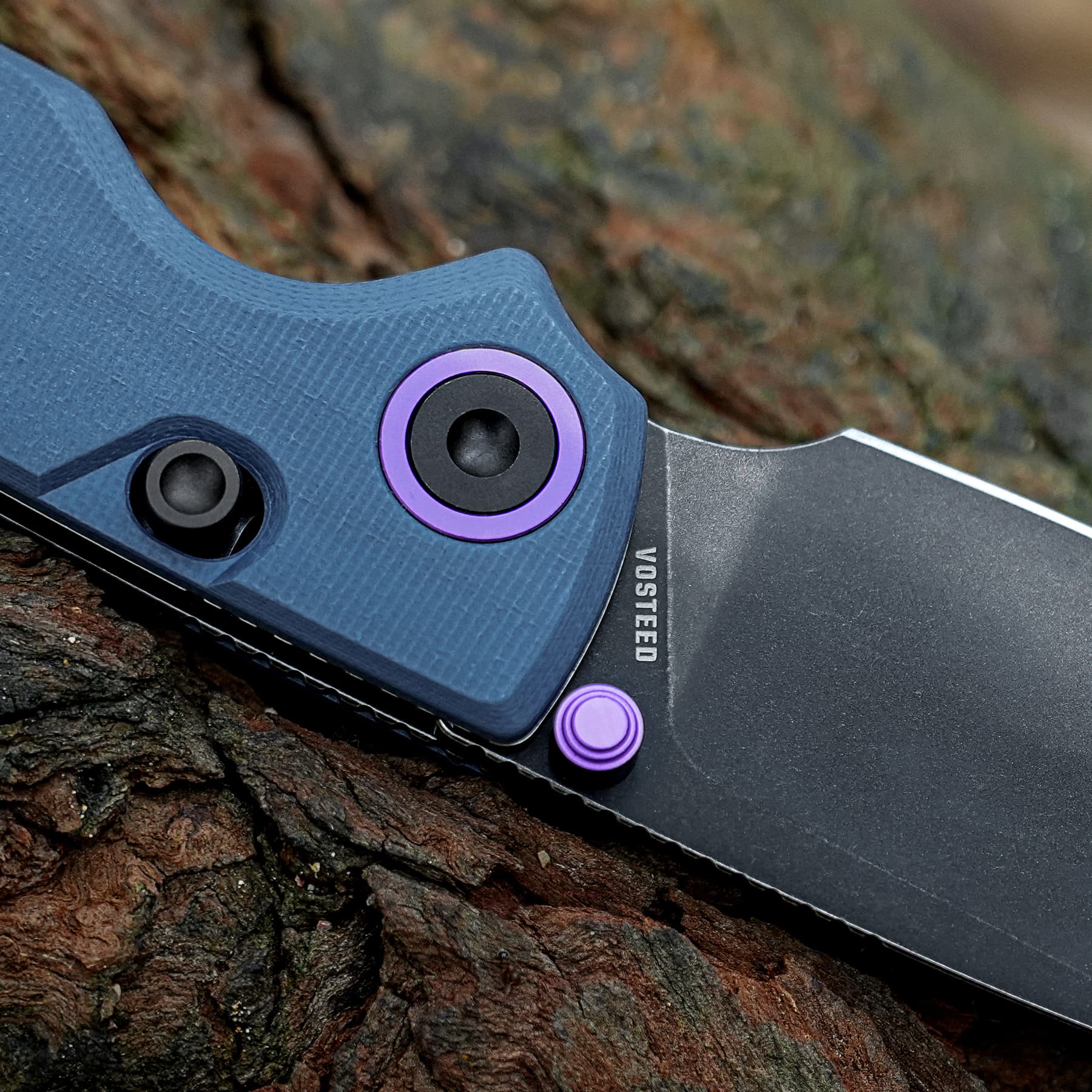 Close-up of a blue textured folding knife handle with purple accents resting on rough tree bark.