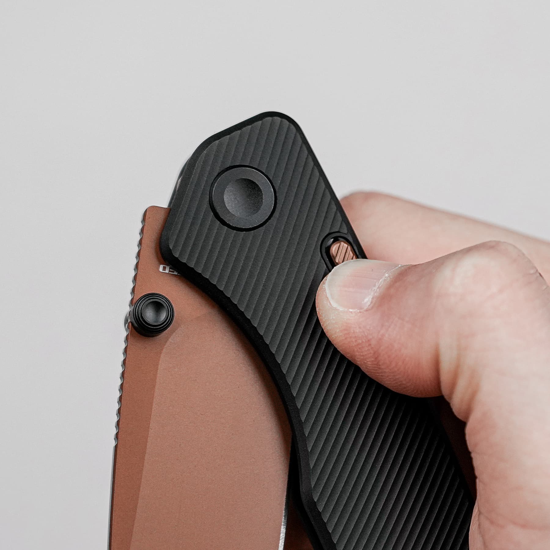 Close-up of a hand holding a folding knife with a black textured handle and brown spacer visible on the side.