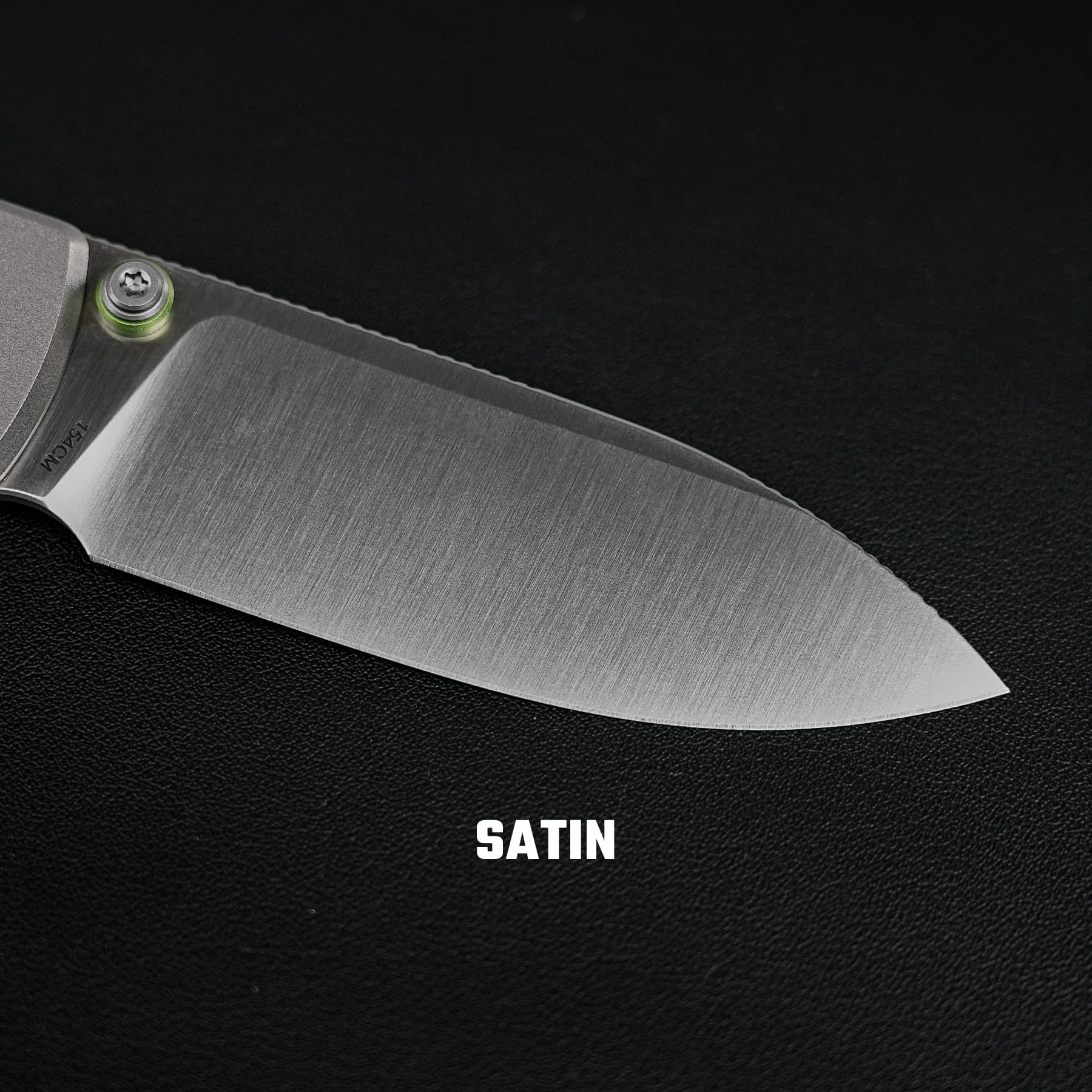 Close-up of a knife blade with a satin finish and a visible green pivot screw near the handle.