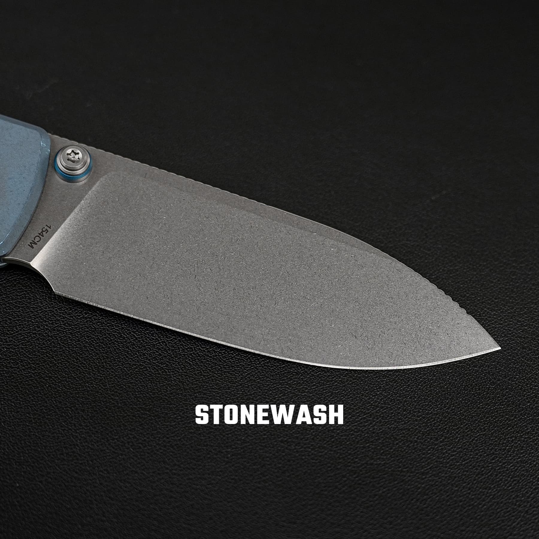 Close-up of a stonewashed knife blade with a blue pivot on a dark textured background, brand name partly visible: STONEWASH