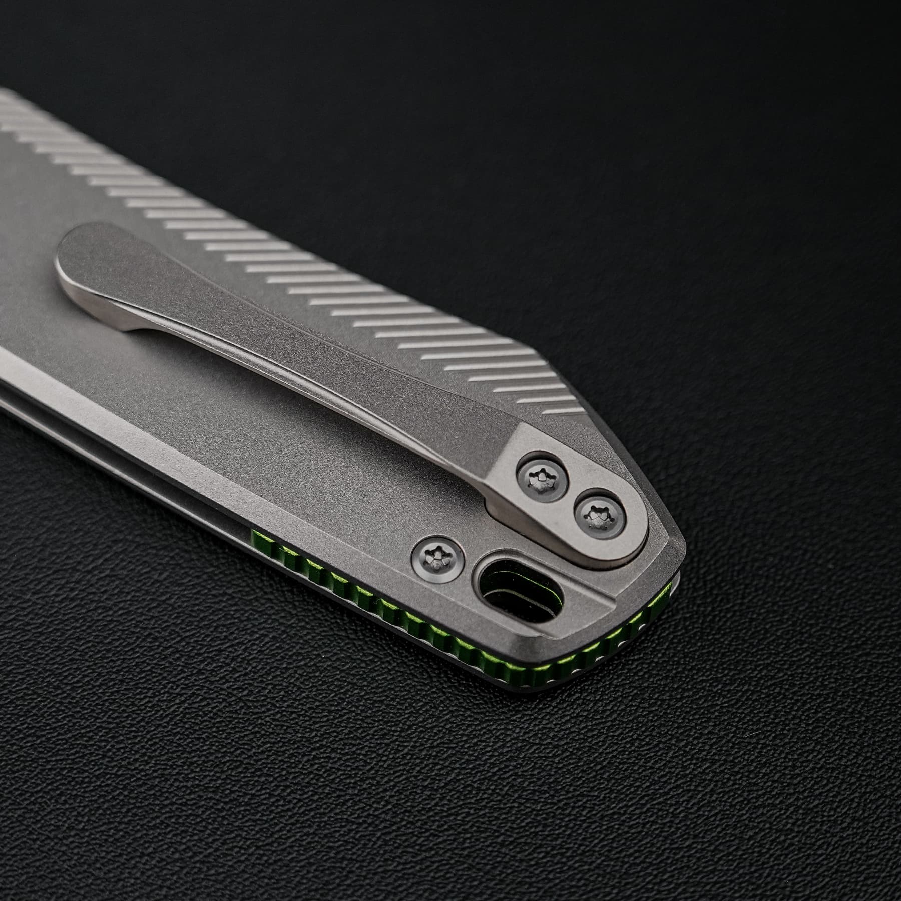 Close-up of a silver folding knife handle with a textured grip and visible screws on a dark surface.