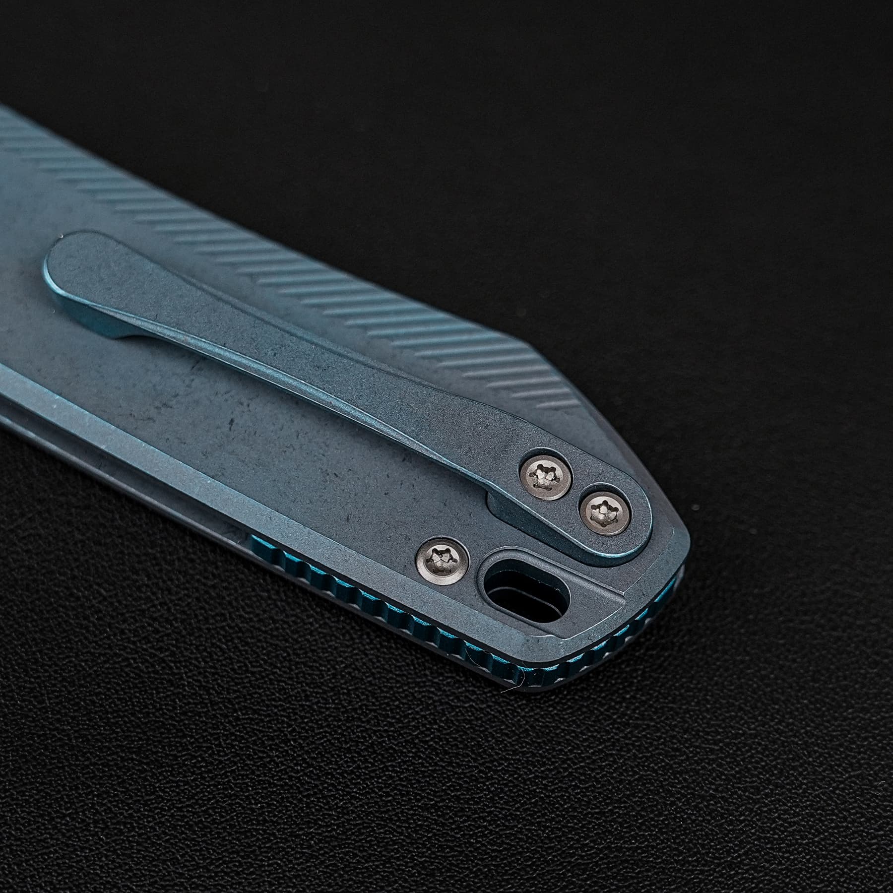 Close-up of a metal multitool with teal accents and visible screws on a dark surface.