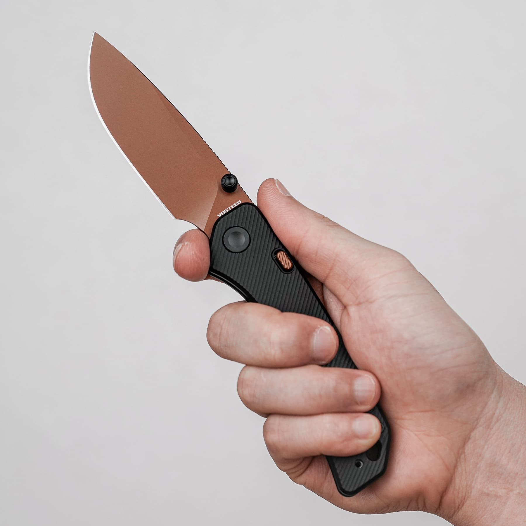 Close-up of a hand gripping a brown-coated folding knife against a gray background.