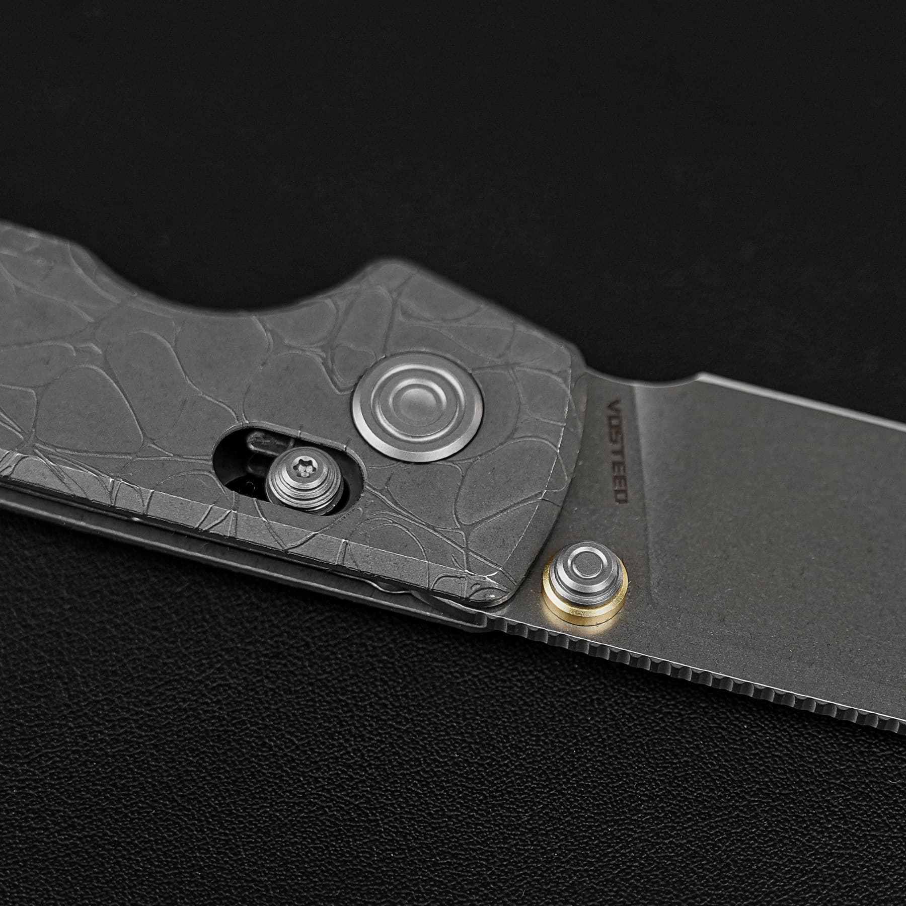 Close-up of a textured knife handle with visible screws and a circular pivot on a dark surface.