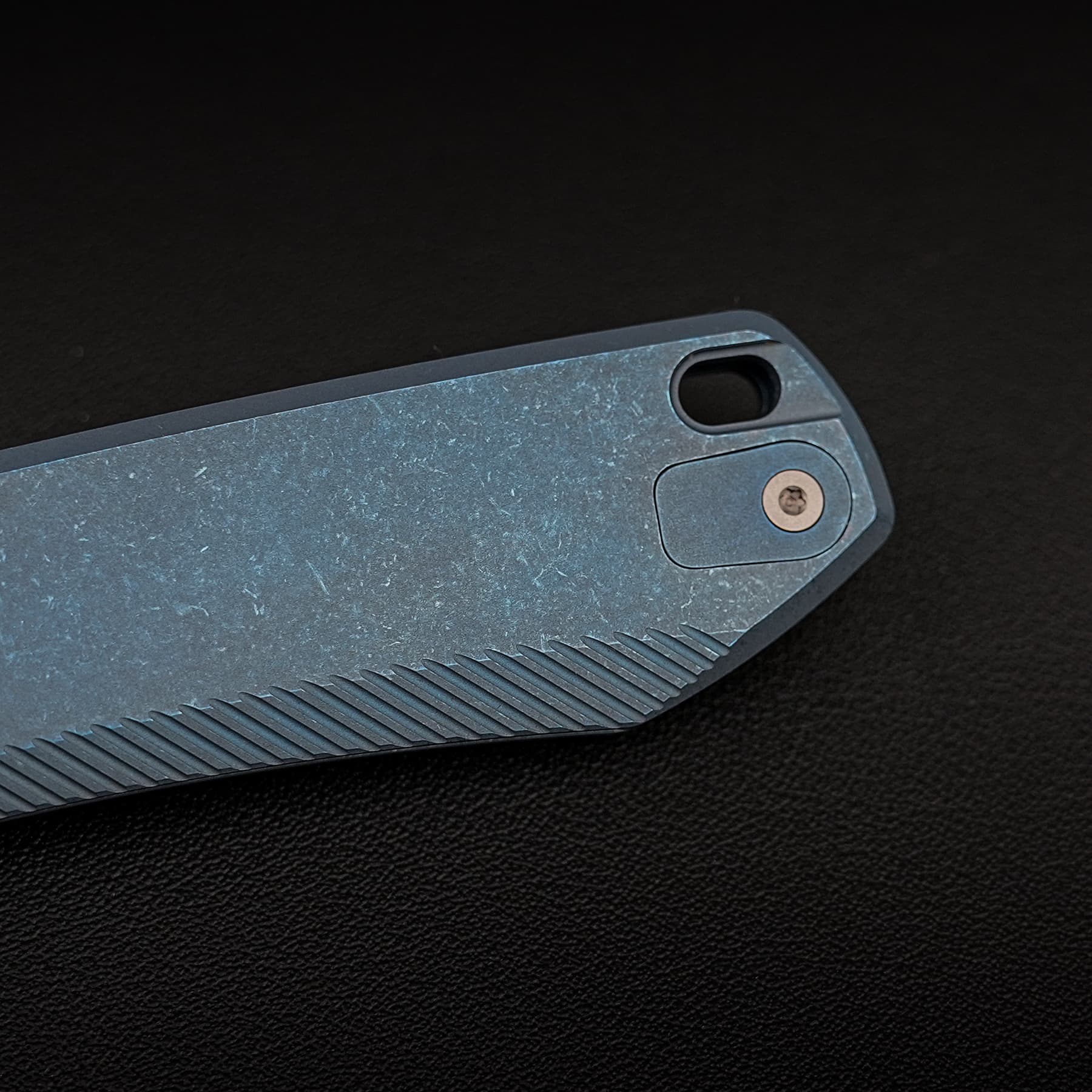 Close-up of the bottom edge of a blue-gray electronic device, showing a textured grip and a circular port on a dark surface.