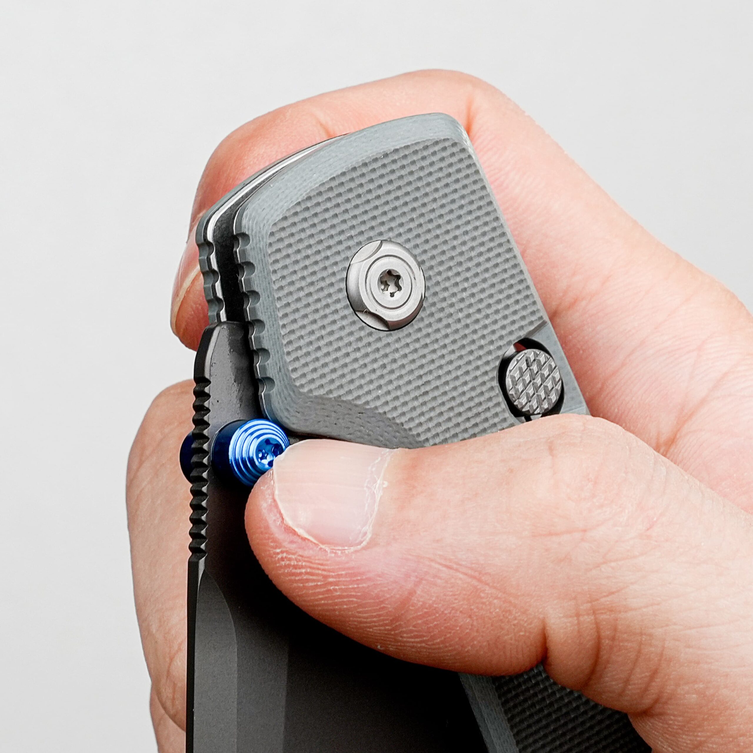Close-up of a hand gripping a gray textured utility knife with the blade partially visible and screws on the handle