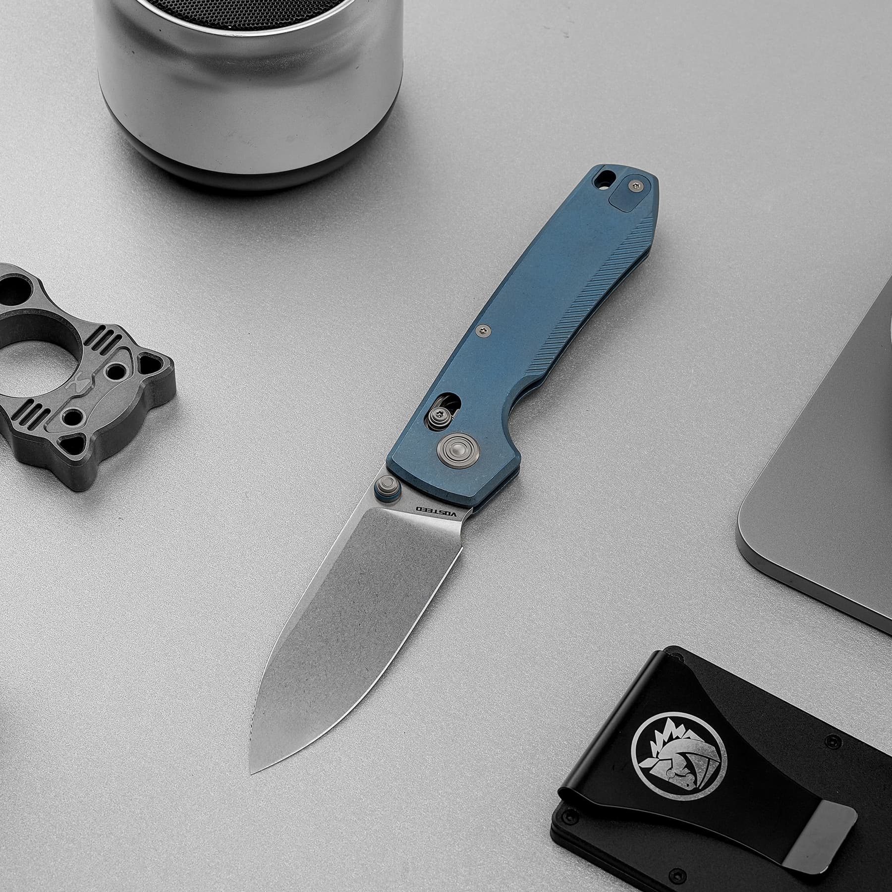 Close-up of a blue utility knife on a gray work surface with other mechanical parts nearby.