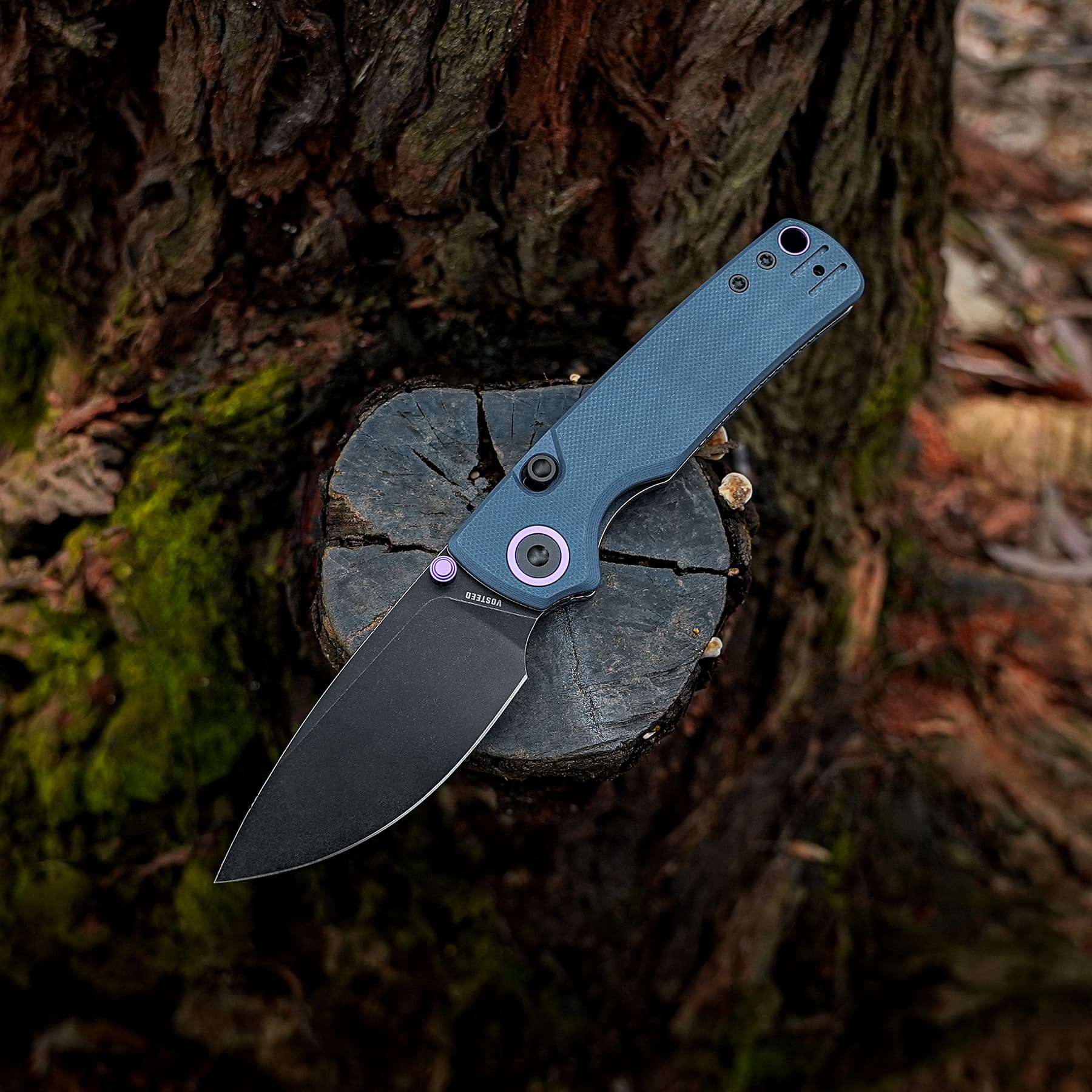 A folding knife stuck into a cut tree stump in a forest, blades exposed against dark wood and mossy ground beside it.