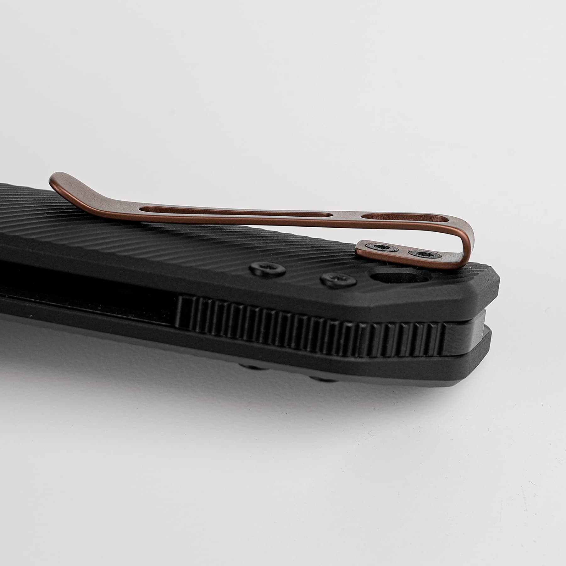 Close-up of a copper-colored metal clip resting on a black ribbed plastic surface with screws nearby.