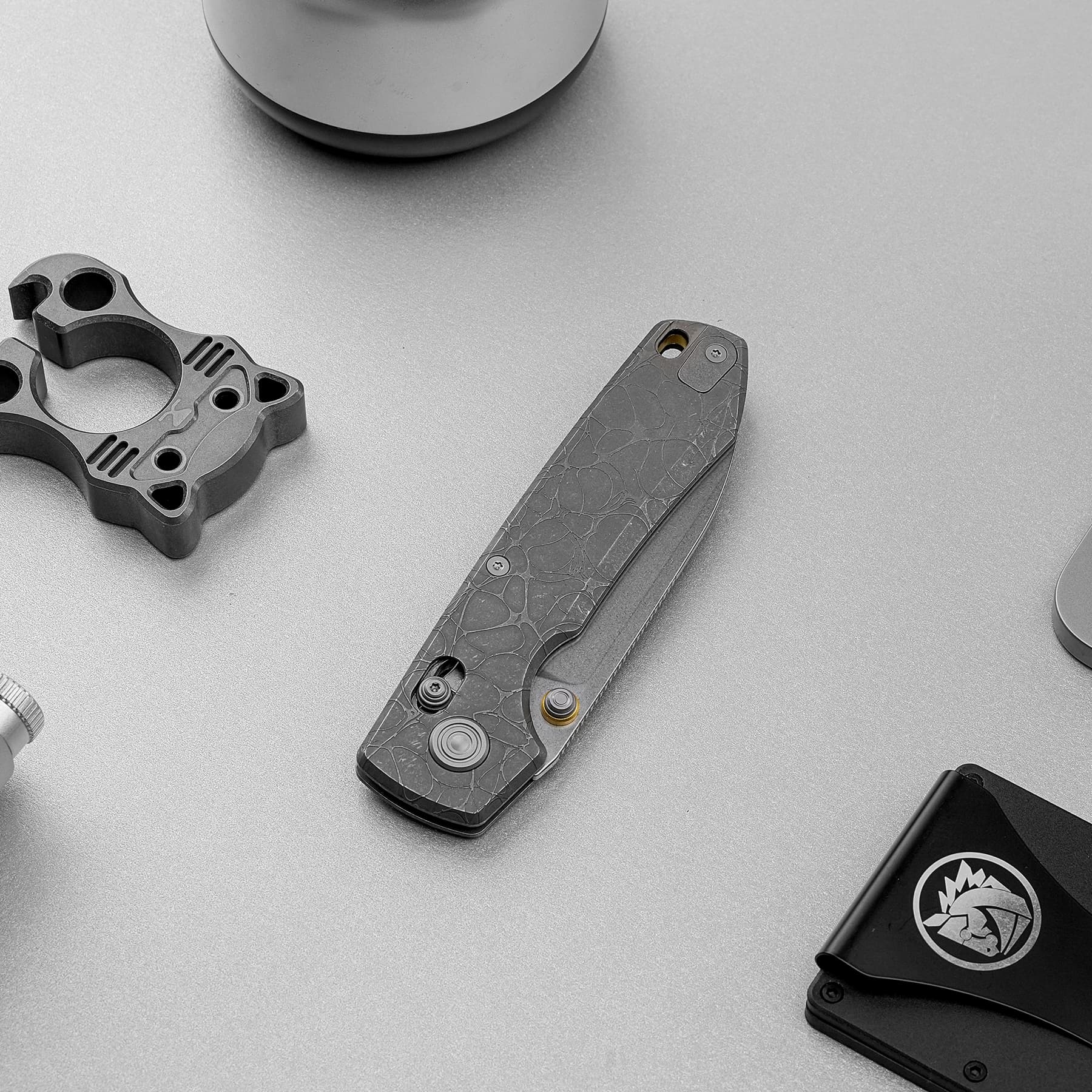 Close-up of a textured folding knife handle and metal components on a gray surface.