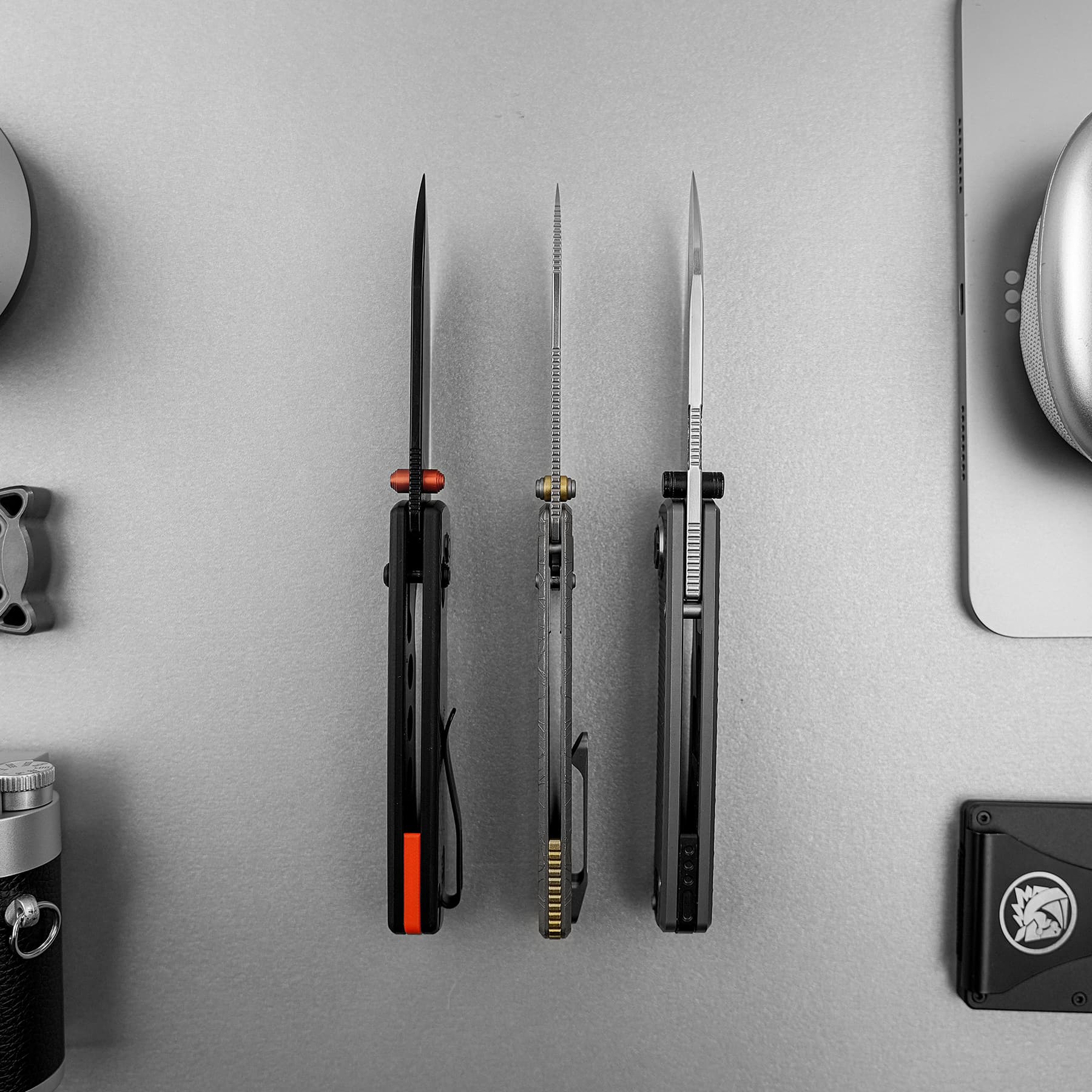 Three precision knives with different blade shapes mounted vertically on a wall in grayscale