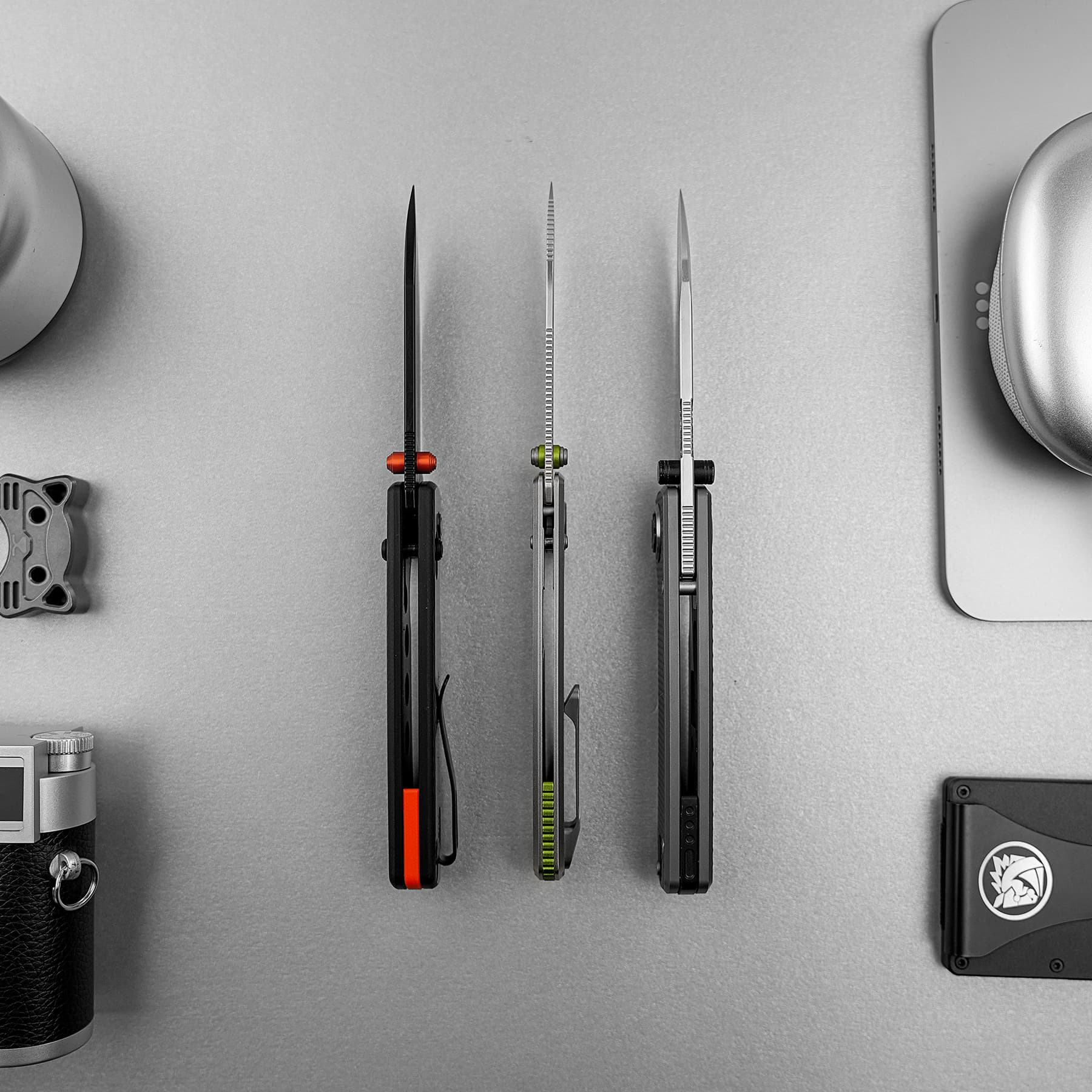 Three vertical craft knives with colored handles mounted on a gray wall, viewed from above the bench area.