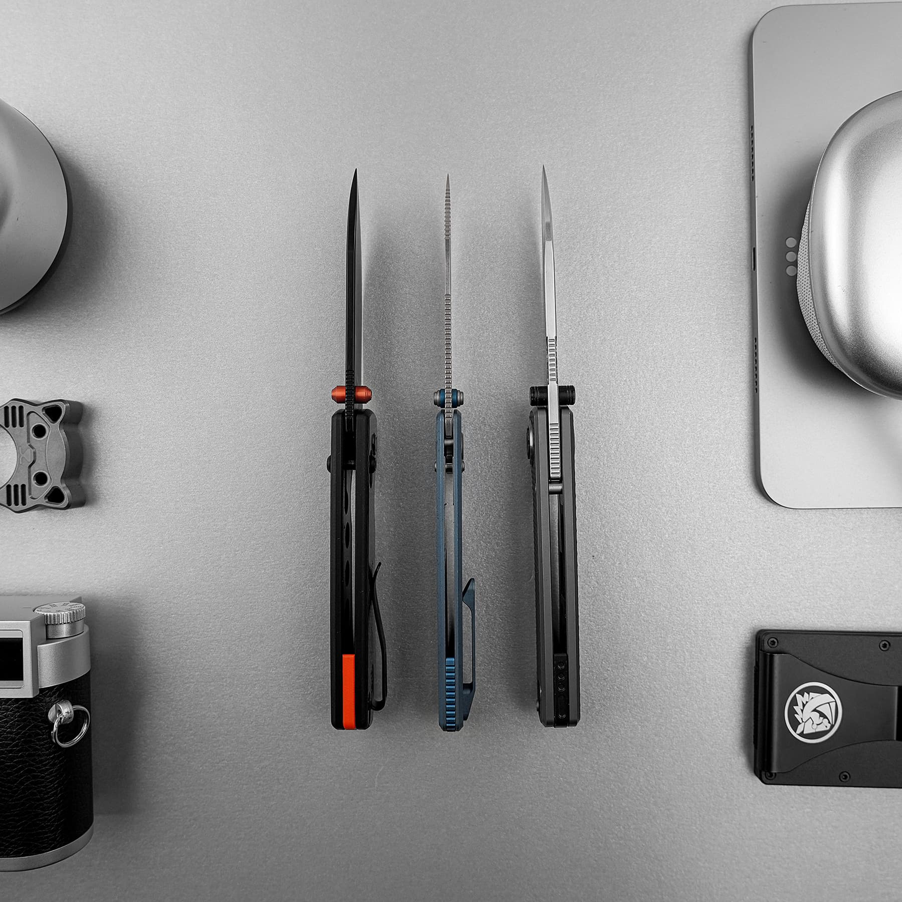 Three precision knives with colored handles stand upright on a gray work surface, laptop edge visible on the right.
