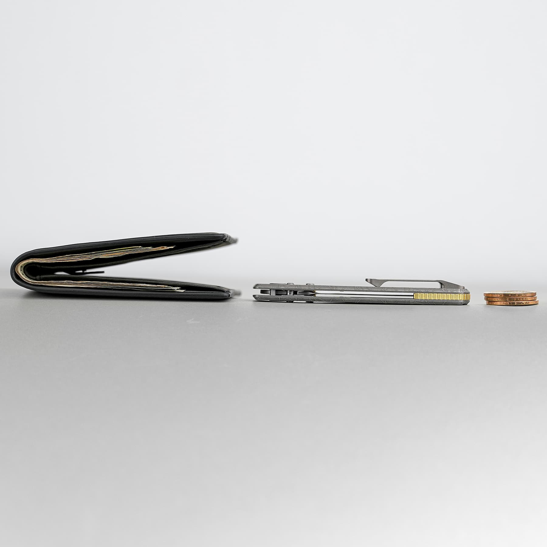 Open black wallet on a gray surface with visible cash, beside a metal money clip and a small stack of coins.