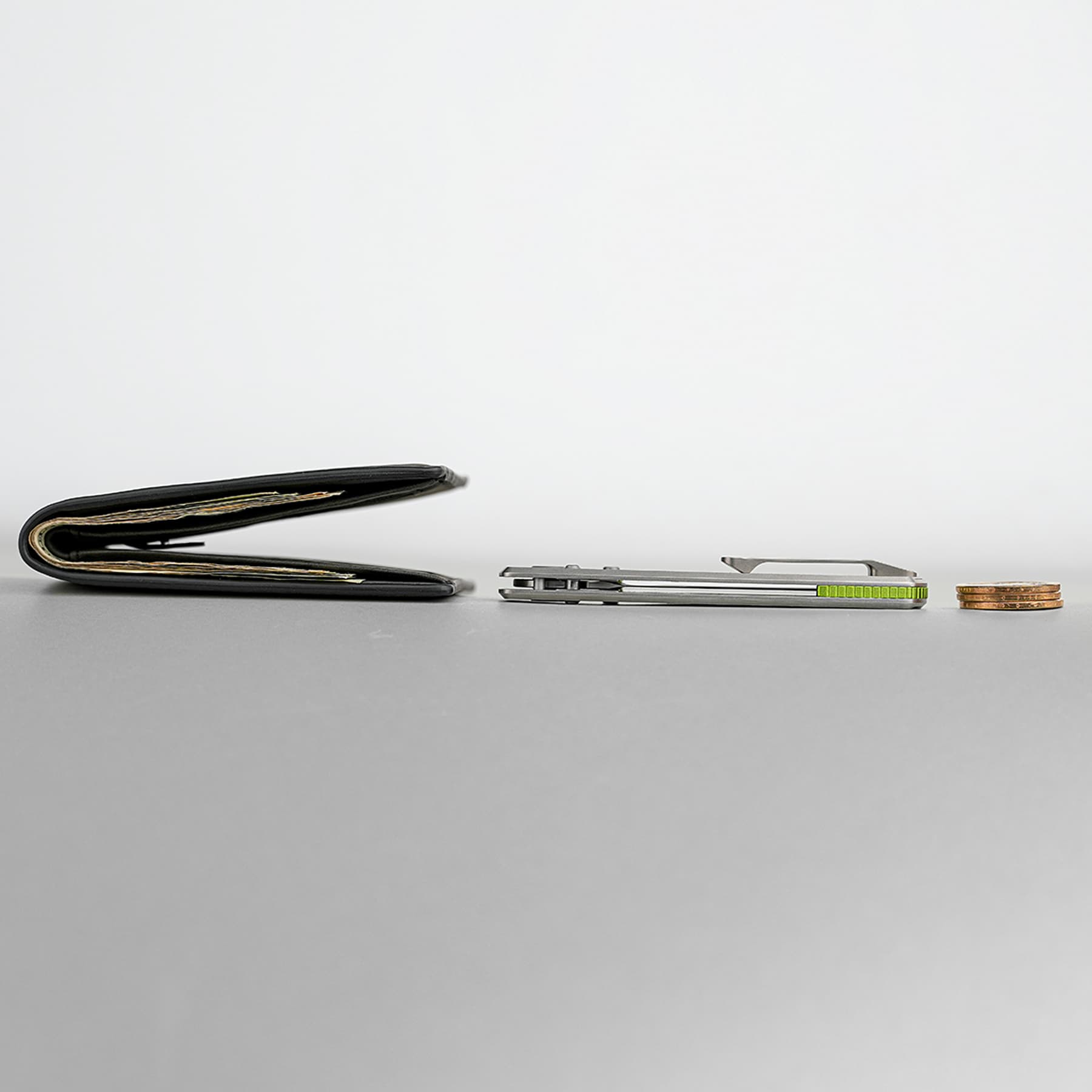 Opened black wallet on a gray surface with visible cards; a metal cardholder and a small stack of coins sit to the right.