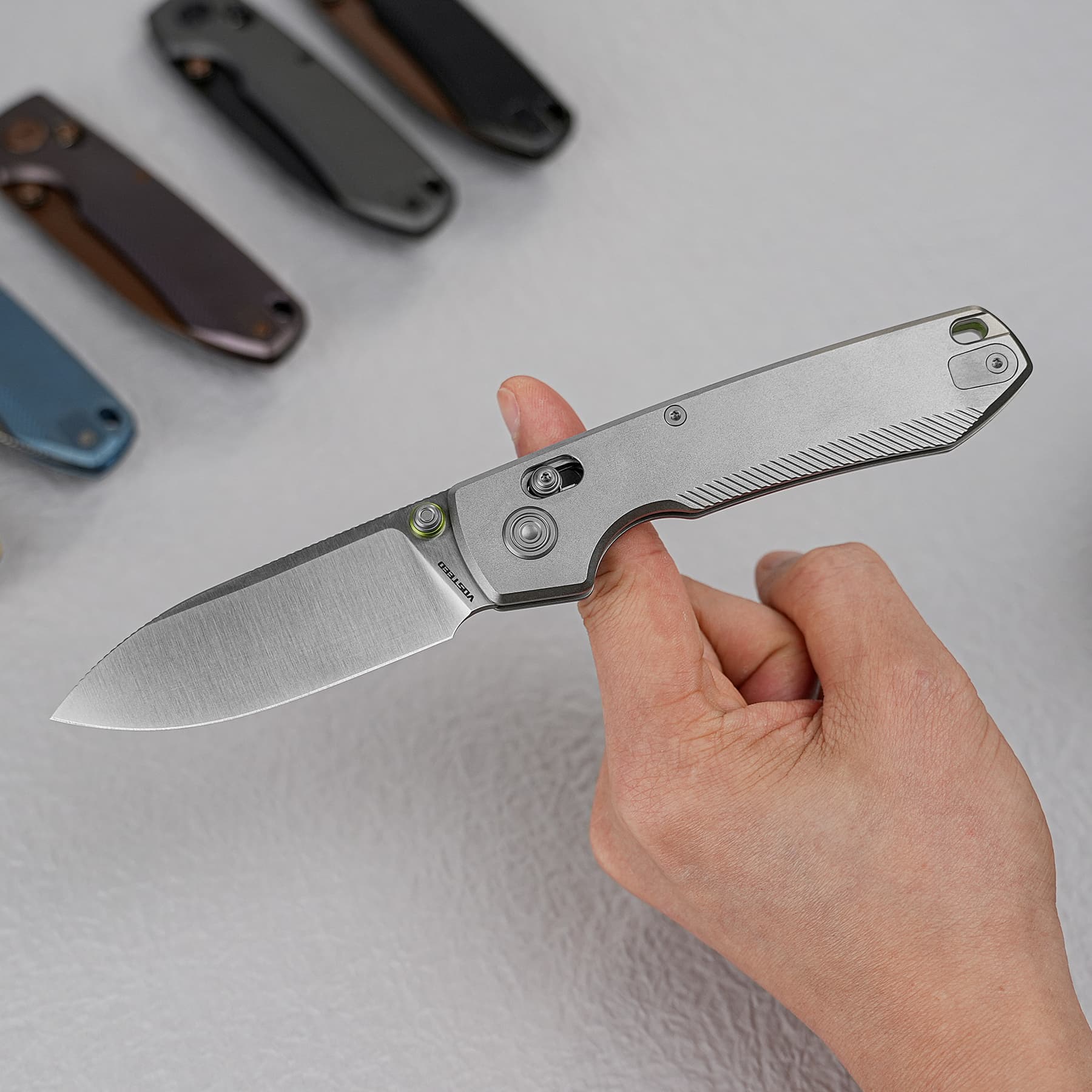 Close-up of a hand holding a silver folding pocket knife, with three other folded blades blurred in the background.