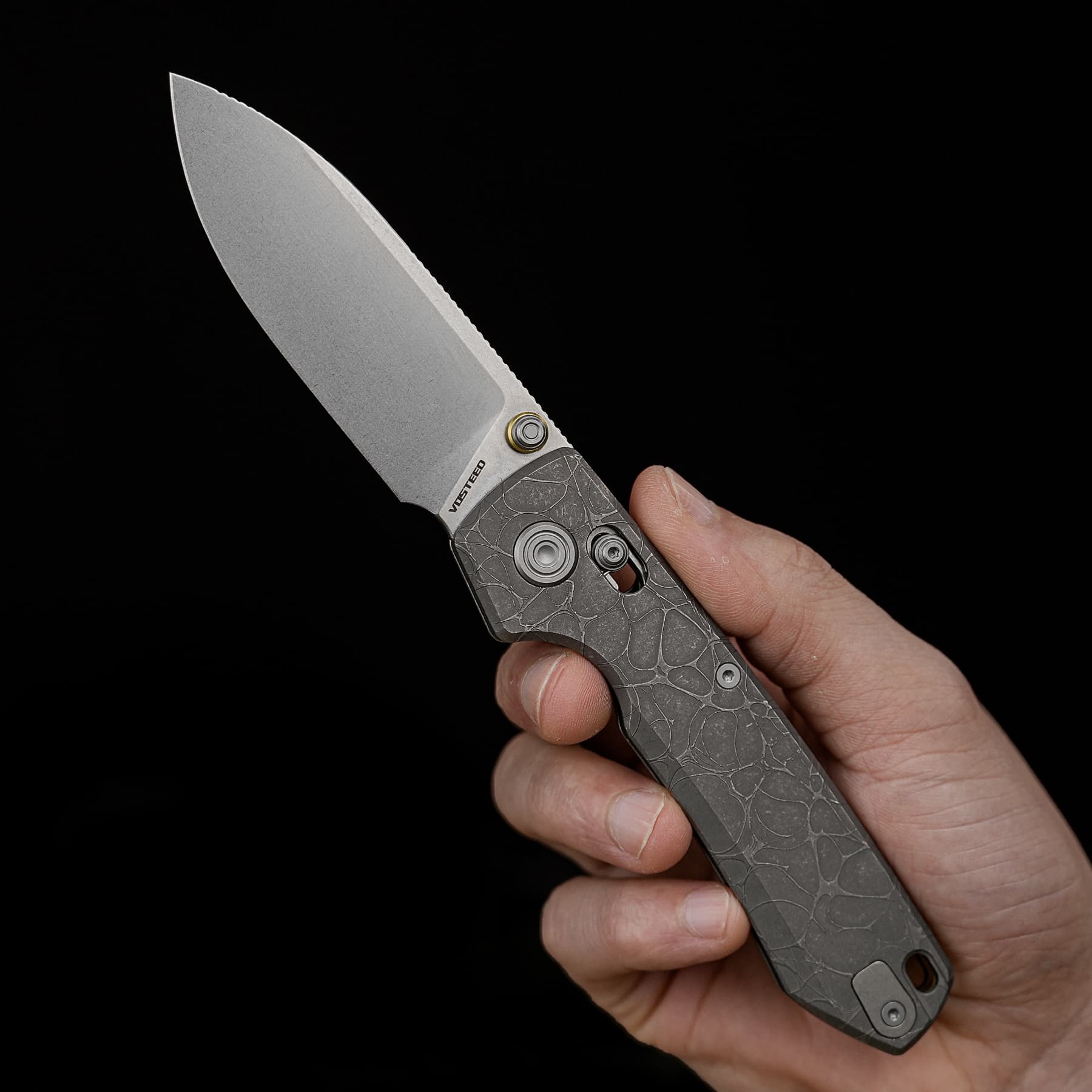 Close-up of a gray folding knife blade partially opened, held by a hand against a black background.