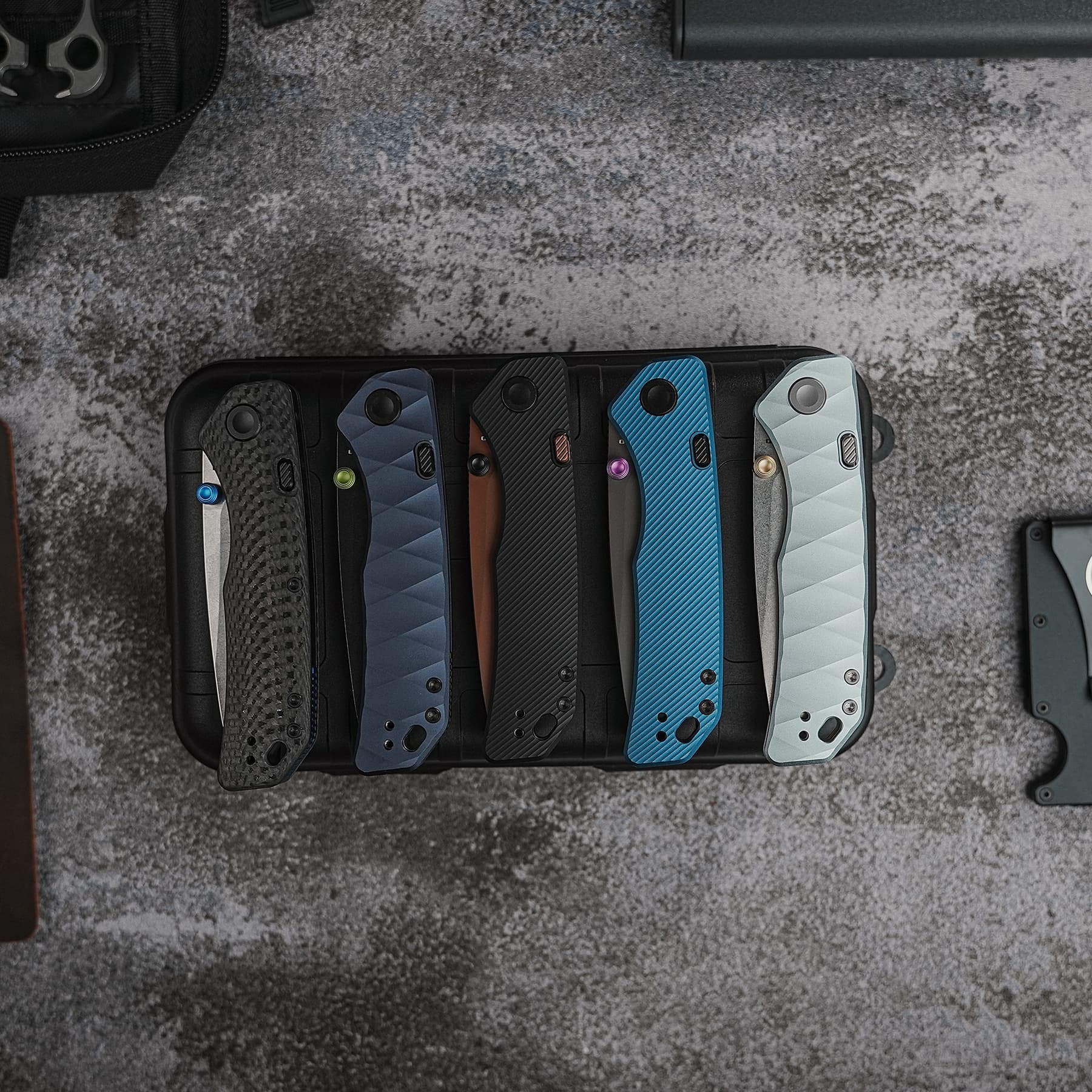 Row of colorful smartphone cases arranged on a black tray, featuring textured patterns in blue, gray, and black tones with metal buttons visible.