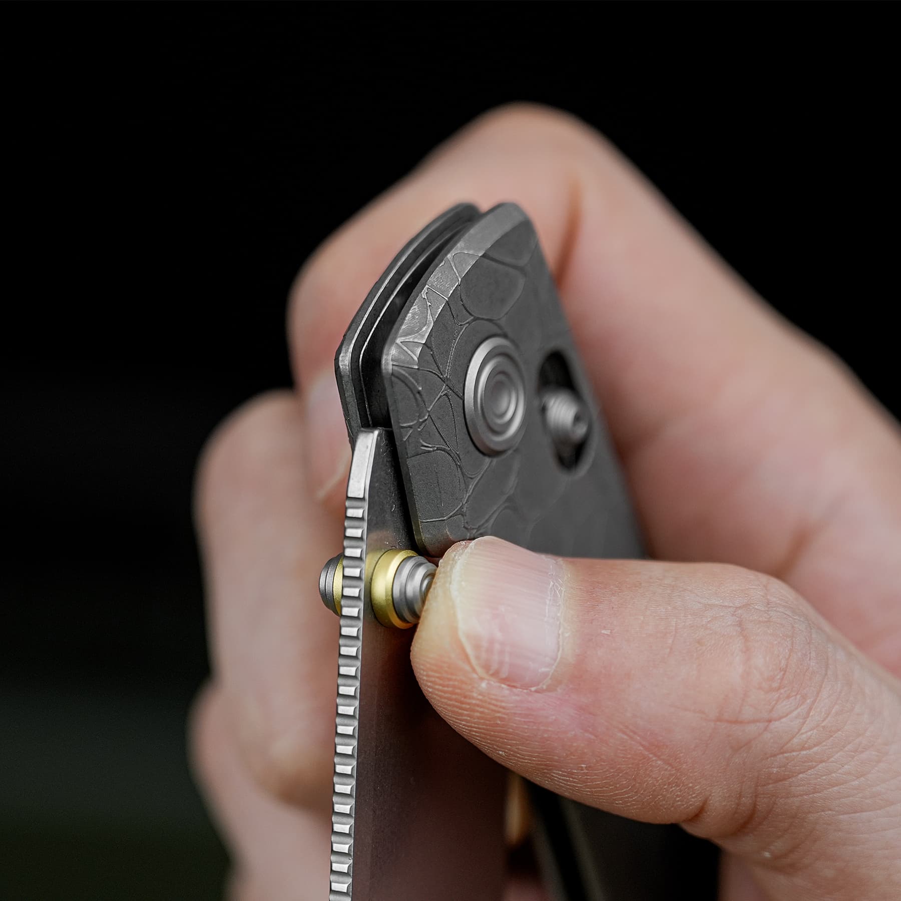 Close-up of a hand prying apart a small textured black device, exposing a circular metal component.