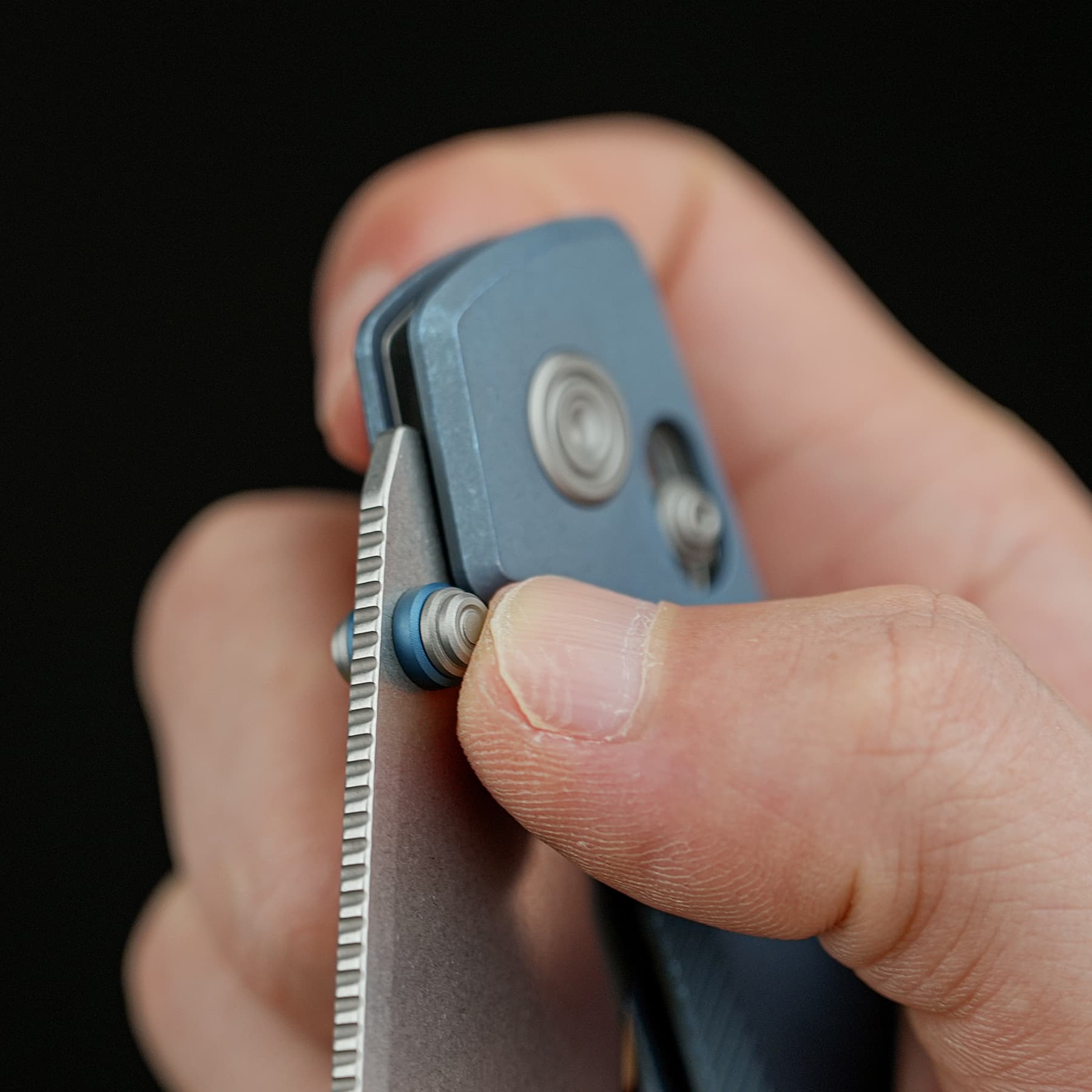 Close-up of a blue folding tool being operated between fingers, showing a round pivot and knurled edge.