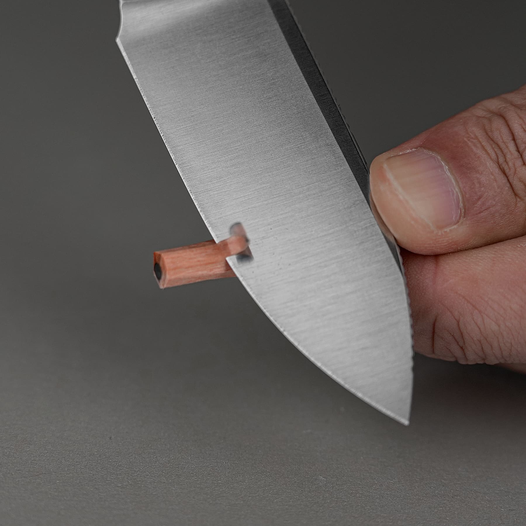 Close-up of a hand gripping a shiny metal blade with a small orange component at the base against a dark background.