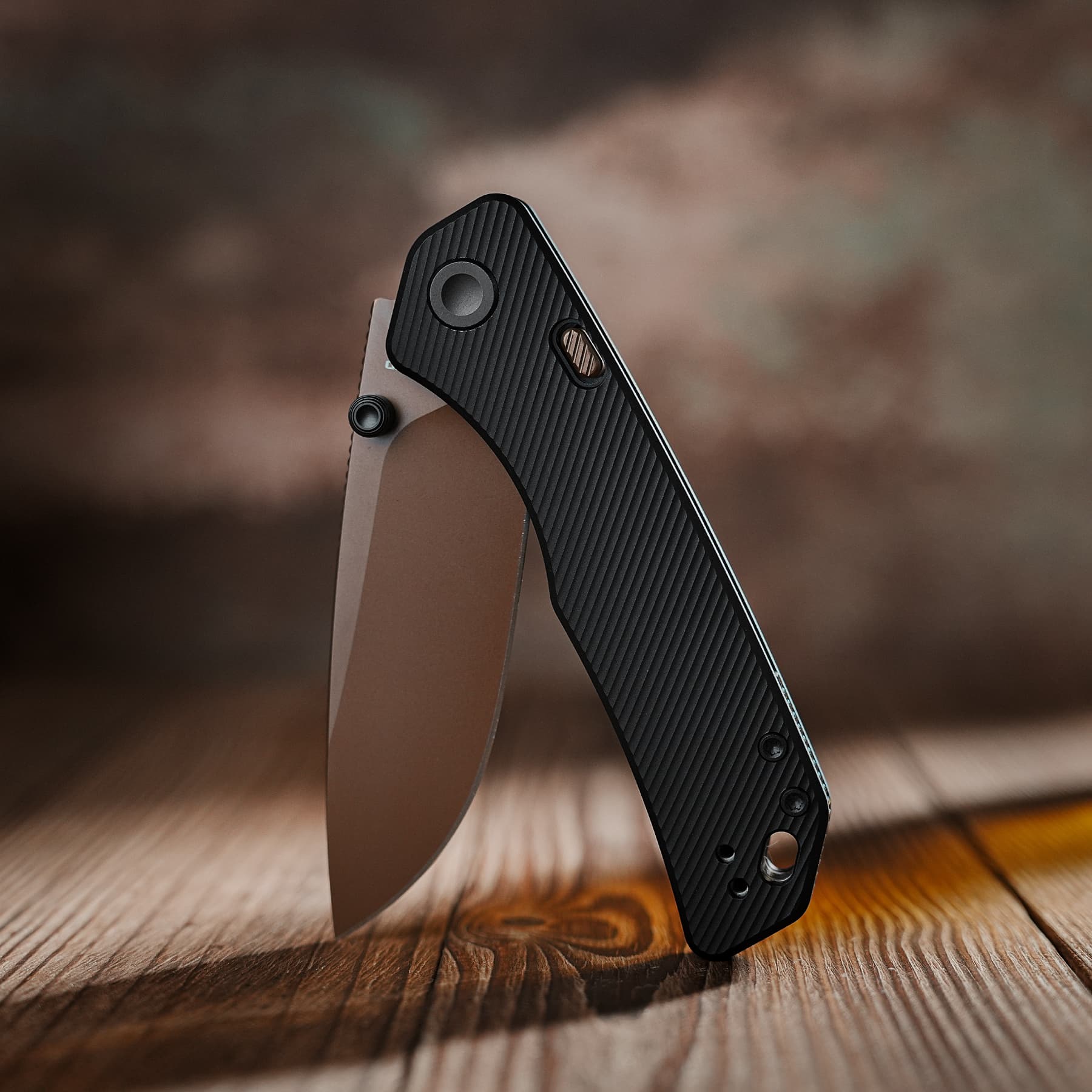 Close-up of a black textured folding knife handle resting on a tan sheath, angled against a wooden surface.