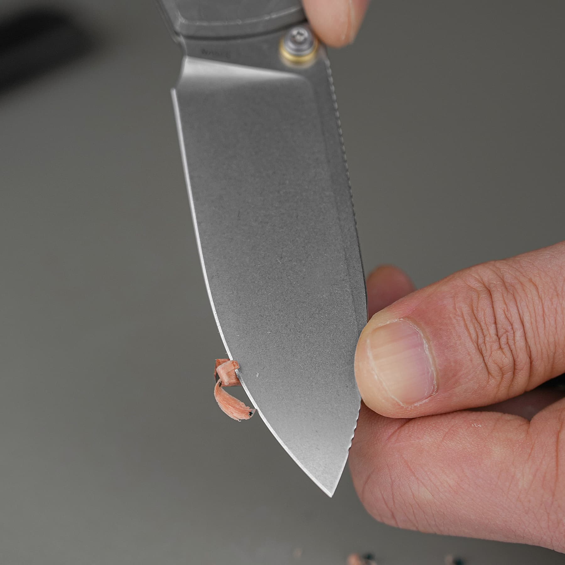 Close-up of a hand holding a metal knife blade with a small curled orange strip attached near the tip.