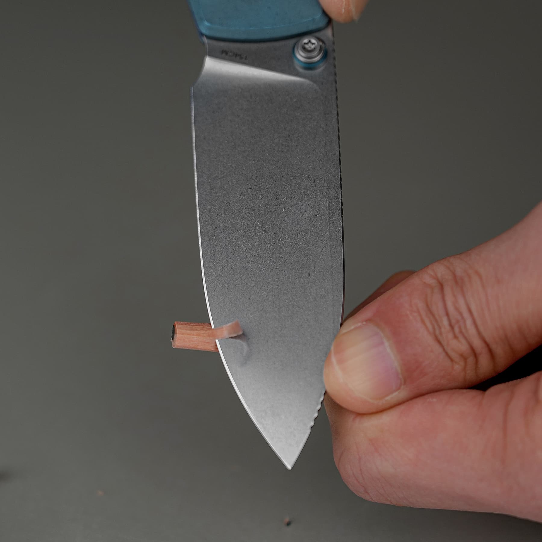 Close-up of a hand holding a metal blade; a copper strip is being shaved or cut from a small copper piece at the blade's edge.