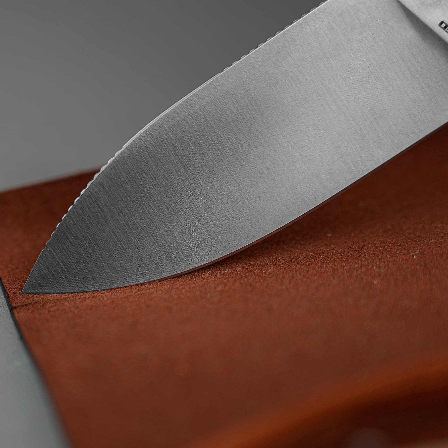 Close-up of a stainless steel knife blade with a serrated edge resting on a brown leather surface.