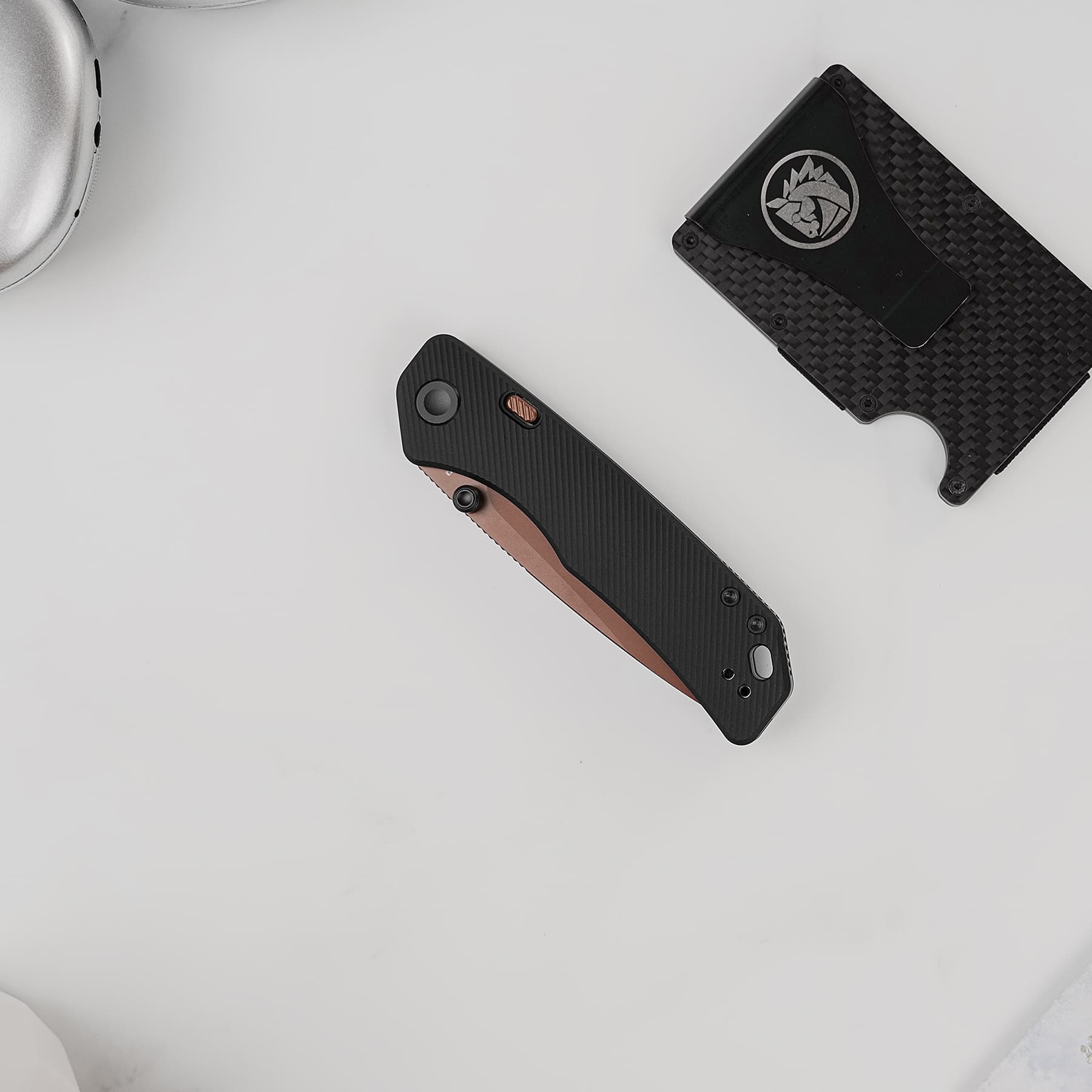 Two folding knives on a light gray surface, showing textured black and brown handles with metal hardware visible in the corners.