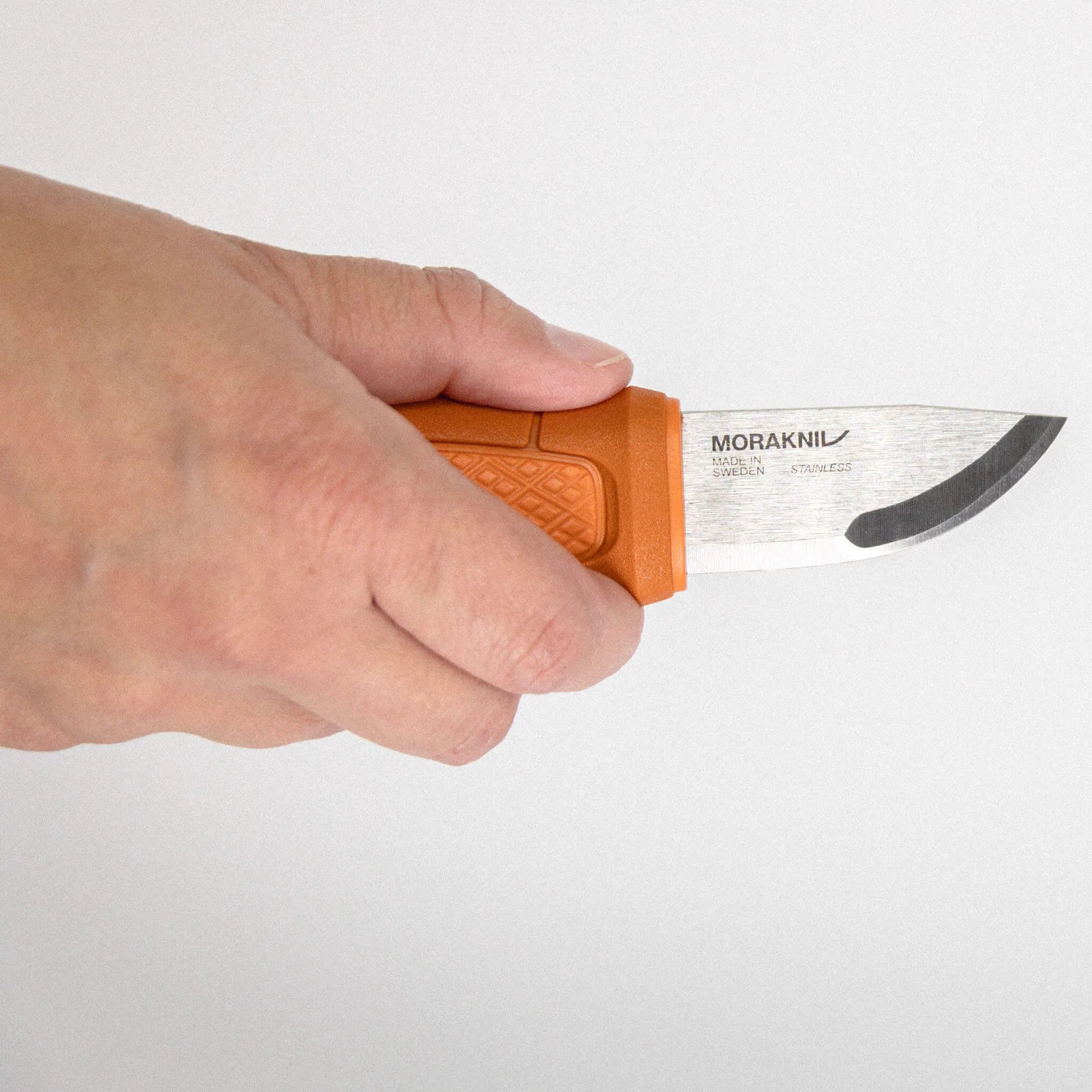 Close-up of a hand holding an orange Morakniv knife with the blade exposed at the edge.