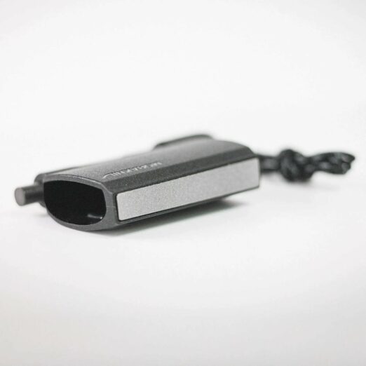 Close-up of a black rectangular electronic device on a white surface, with a cord extending to the right in the background.