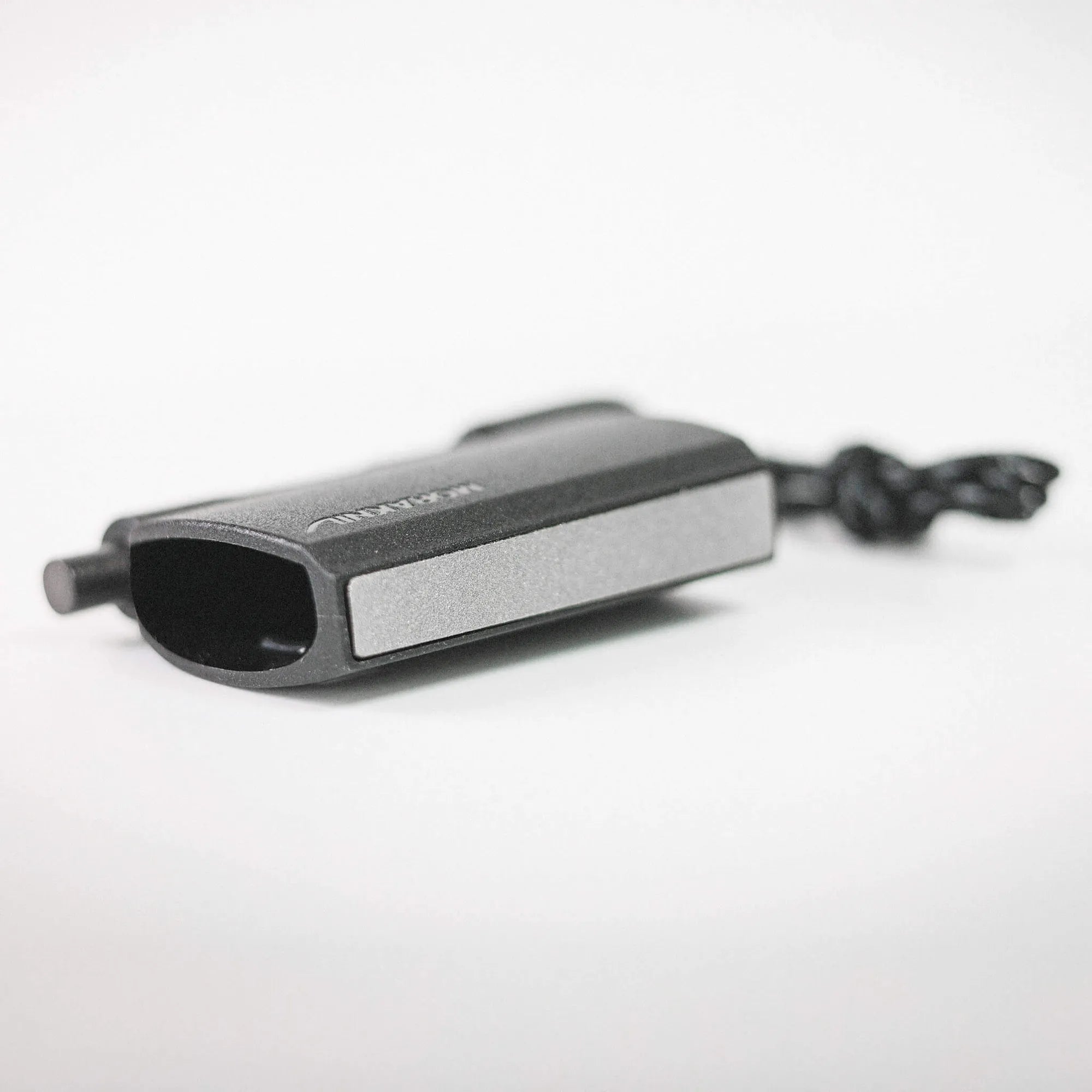 Close-up of a black rectangular electronic device on a white surface, with a cord extending to the right in the background.