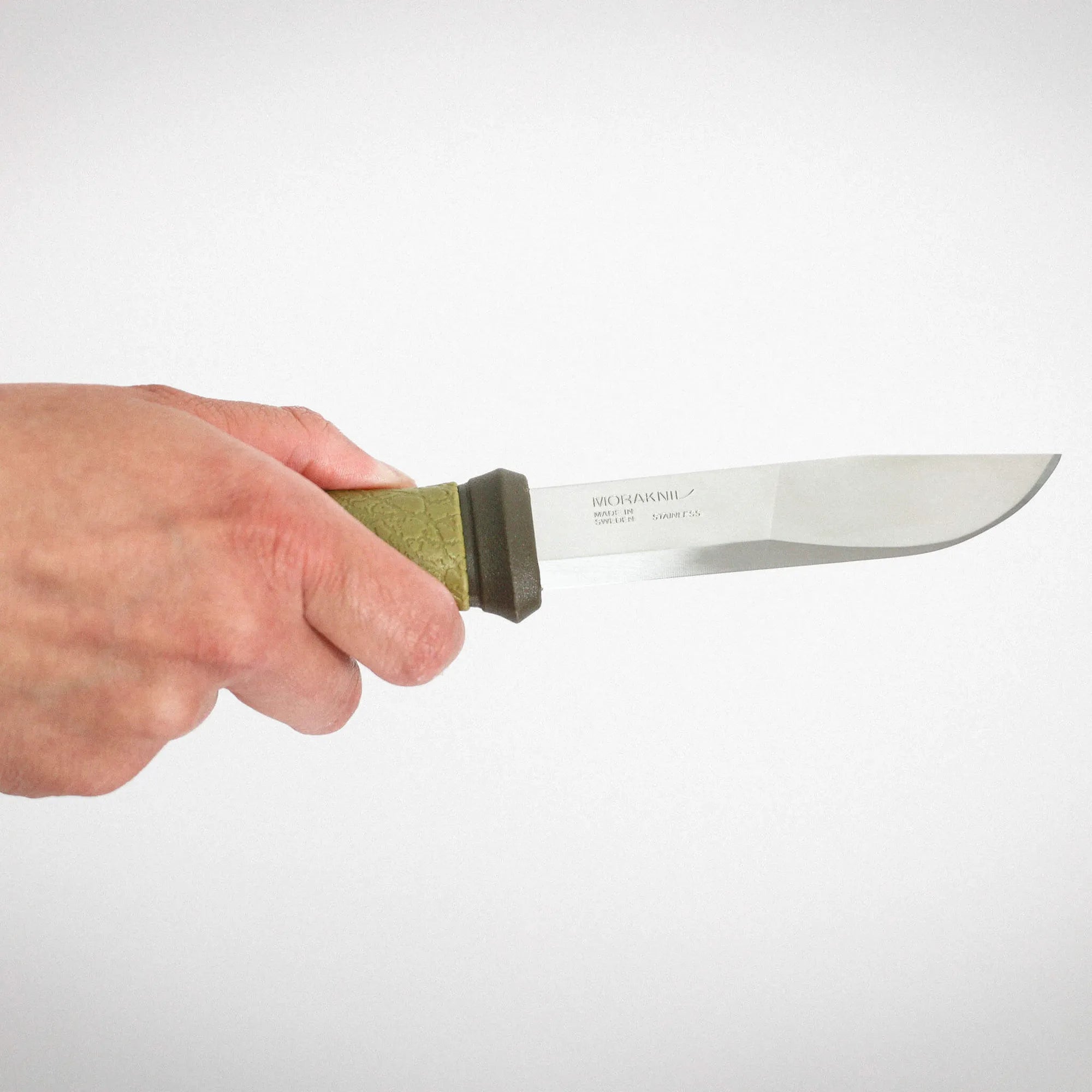 Close-up of a hand gripping a Morakniv fixed-blade knife with a green textured handle, blade extending to the right.